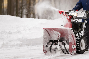 A man with a red snow-covered snow blower clears the area from snow. Clearing the area from...