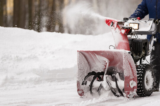 A man with a red snow-covered snow blower clears the area from snow. Clearing the area from snowfall.