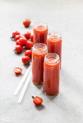 Tomato juice in a tall glass bottles with a straws on a light gray background