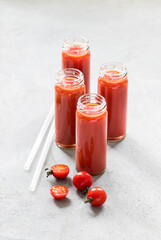 Cherry tomato drink in tall glass bottles with straws on a light gray background
