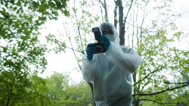 Criminalists taking pictures at crime scene in forest, using professional photo camera, taking evidence from accident. Investigating proofs, forensic examination. Detective workers, medical examiners