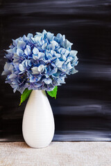 Hydrangea flowers in a vase against a black painted background; Simple arrangement of bouquet against a dark background