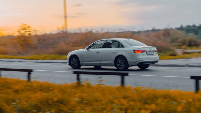 Audi A4 B9 driving on the country road at dusk. Side view of white sedan in motion on the background of autumn nature