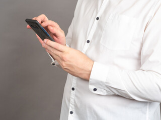 Hands of man with phone. Businessman in shirt holds cellphone. Male dials number into cellphone. Man is typing message. Human works with some apps in phone. Concept mobile applications for business