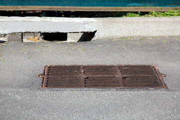 drainage grate on a rectangular manhole on an asphalt road with a storm ditch canal in the curb...