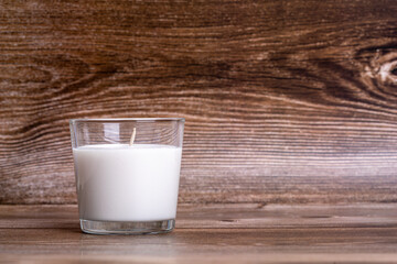 Aromatic scented candle in glass on the wooden background. Create relaxed atmosphere. Preparing for romantic dating. Postcard composition with free space for text. New Year and Christmas concept.