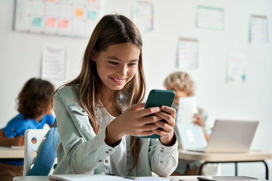 Happy latin hispanic kid girl school student using smartphone in classroom. Preteen child holding mobile cell phone having fun with apps playing games and checking social media at school during break.