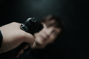 First person view of gun aimed at young man on black background. Firearm in man's hand. POV of...