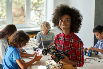 Happy African American junior school kid holding robotic car looking at camera at STEM class....