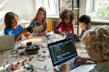 Diverse school children students build robotic cars using computers and coding. Happy multiethnic...