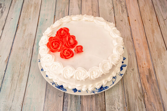 Delicious Complete Peach Sponge Cake With White Cream Topping And Edible Red Roses On A Plate With Blue Flowers