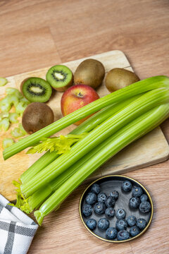 Image of vegetable ingredients to prepare a detox juice. Ripe blueberries, celery stick, delicious kiwis and digestive red apples