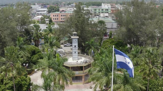 Toma aérea de bandera de Honduras ondeando cerca del reloj antiguo del parque, El Progreso, Yoro