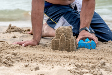 Dad makes a sand castle on the beach using plastic  molds 