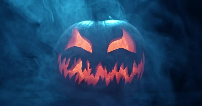 Spooky Halloween jack o lantern with glowing scary face carved out of a pumpkin and surrounded by smoke and mist.