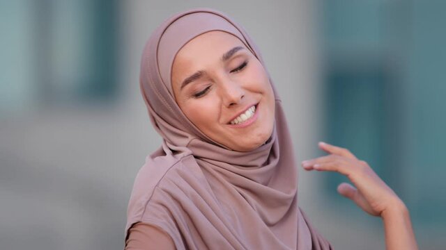 Portrait of beautiful young Arab muslim woman in traditional hijab dancing in city smiling. Close up female face with smile islam girl islamic arabian lady dance with music moving movement outdoors