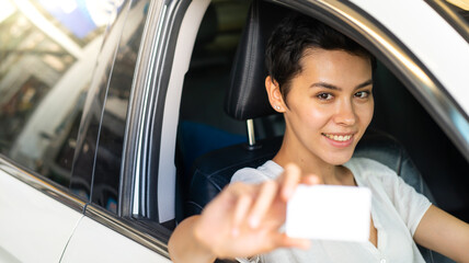 Confident young woman driver in car holding blank card mockup. Caucasian woman showing new driver's...