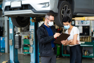 Mechanic man and woman customer wearing medical face mask protection coronavirus and check the car condition before delivery.