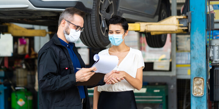 Mechanic man and woman customer wearing medical face mask protection coronavirus and check the car condition before delivery. - Powered by Adobe