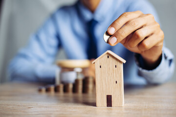 Business hand holding home with Buy or Rent, copy space. Property investment and house mortgage financial concept, Hand putting money coin stack with wooden house.