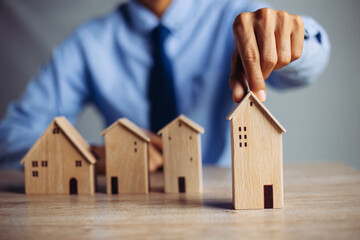 Businessman choosing mini wood house model from model on wood table, Planning to buy property....