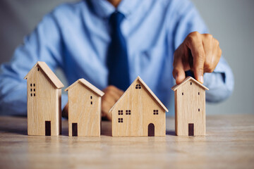 Businessman choosing mini wood house model from model on wood table, Planning to buy property. concept of Choose the best.