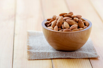 Almonds in brown bowl on wooden background