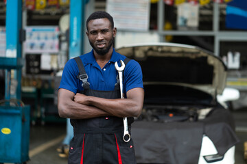 Portrait of attractive African man arm cross look camera and big wrench tools in hand. Expertise mechanic working in automobile repair garage.