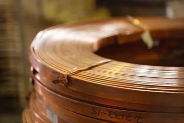 Foto op Plexiglas Rolls of flat copper products close-up. Copper tape in bundles. Copper rolling. © Anton