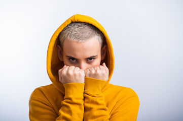 Young woman in ocher hood holding fists near face on white background.