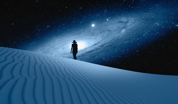 Silhouette of woman walking on the sand dune - Amazing view of the blue desert under the night starry sky with Andromeda galaxy "Elements of this image furnished by NASA"