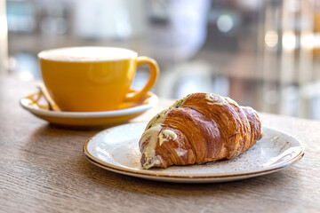 Croissant and cappuccino in yellow cap on a wooden table in a cafe