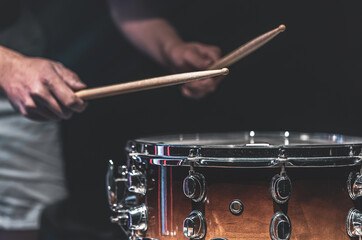 The drummer's hands hold drumsticks and play the snare drum.