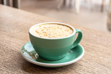 Cappuccino in turquoise cap with latte art on a wooden table