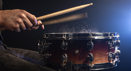 A man plays with drumsticks on a snare drum with splashing water.