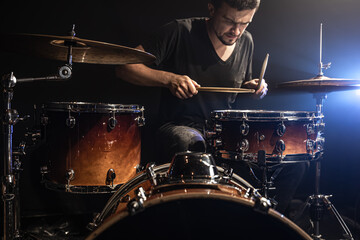 Fototapeta na wymiar A man plays drums on stage in the dark with stage spotlights.