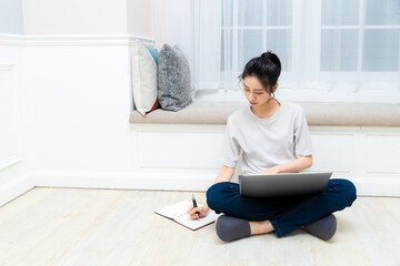 young pretty girl sitting near the window with a laptop, she uses the computer at home on the windowsill, a woman freelance, copy space for text