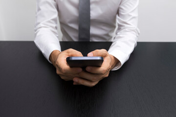 Close up of business man hands using smartphone on a black wood table.