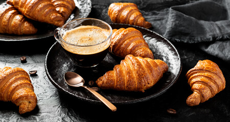 French croissants for breakfast. Freshly baked croissants with cup of coffee on black stone background. Tasty croissants.