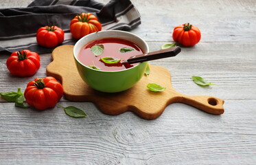 A bowl of fresh gazpacho ,cold tomato soup with basil leaves on gray background