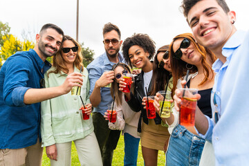 Group of happy young friends with drinks gathered at park