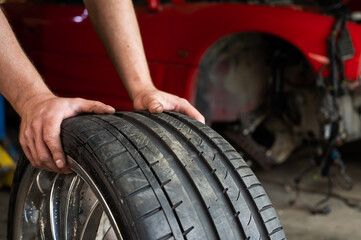 An auto mechanic holds a wheel of a car. Change of car tires according to the season