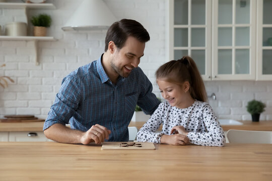 Happy dad teaching excited daughter kid to play learning board game at kitchen table. Cheerful girl thinking over next move in checker draughts, training brain skills, Family smart activity concept