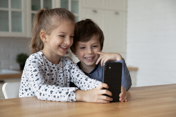 Happy excited sibling gen Z kids using smartphone together, looking at screen, laughing. Children playing virtual game on mobile phone, making video call, watching online funny content on internet