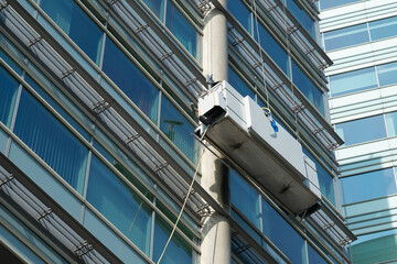 Obraz premium Window cleaners at work at a great height in a gondola at the uwv building in Amsterdam Sloterdijk, Noord-Holland Province, The Netherlands
