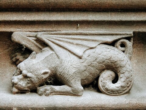 CHESTER, CHESHIRE, UK – JULY 11, 2019: Medieval sandstone ornament depicting a dragon with curled up tail, carved into a decorative frieze on the upper part of the Chester Cathedral facade