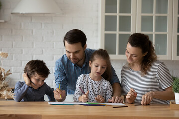 Happy couple teaching sibling kids to draw with color pencils. Parents, preschooler son and daughter standing at table together, enjoying craft activities, developing creative artistic skills