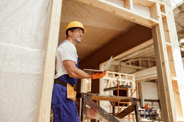 Naklejka na ściany i meble Joyful male builder using laptop at construction site