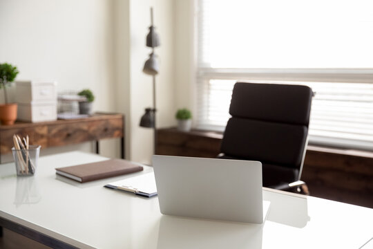 Businessperson Empty Office Workplace With No People, Comfortable Armchair For Work At White Desk With Open Laptop Placed By Window In Pale Colored Room. Modern Business Leader Table With Computer