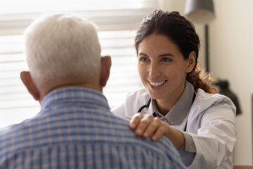 Happy optimistic female GP doctor giving hope and support to senior 80s male patient at...
